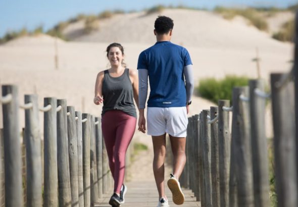 A couple enjoys jogging on a sunny beach boardwalk in Portugal, capturing a moment of fitness and leisure.