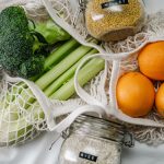 Overhead view of eco bags with broccoli, oranges, and grains in jars, promoting a zero-waste lifestyle.