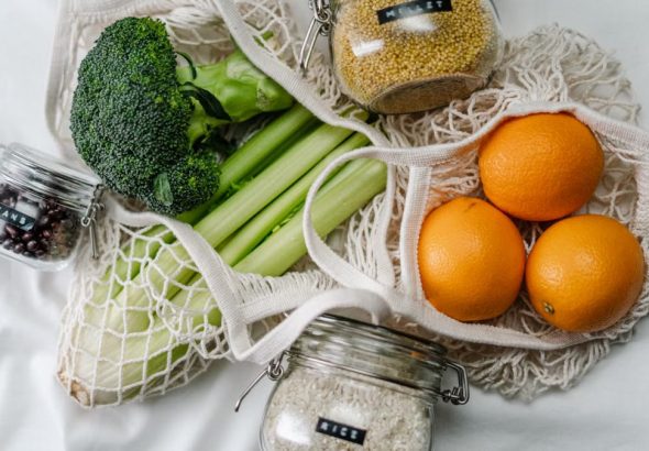 Overhead view of eco bags with broccoli, oranges, and grains in jars, promoting a zero-waste lifestyle.
